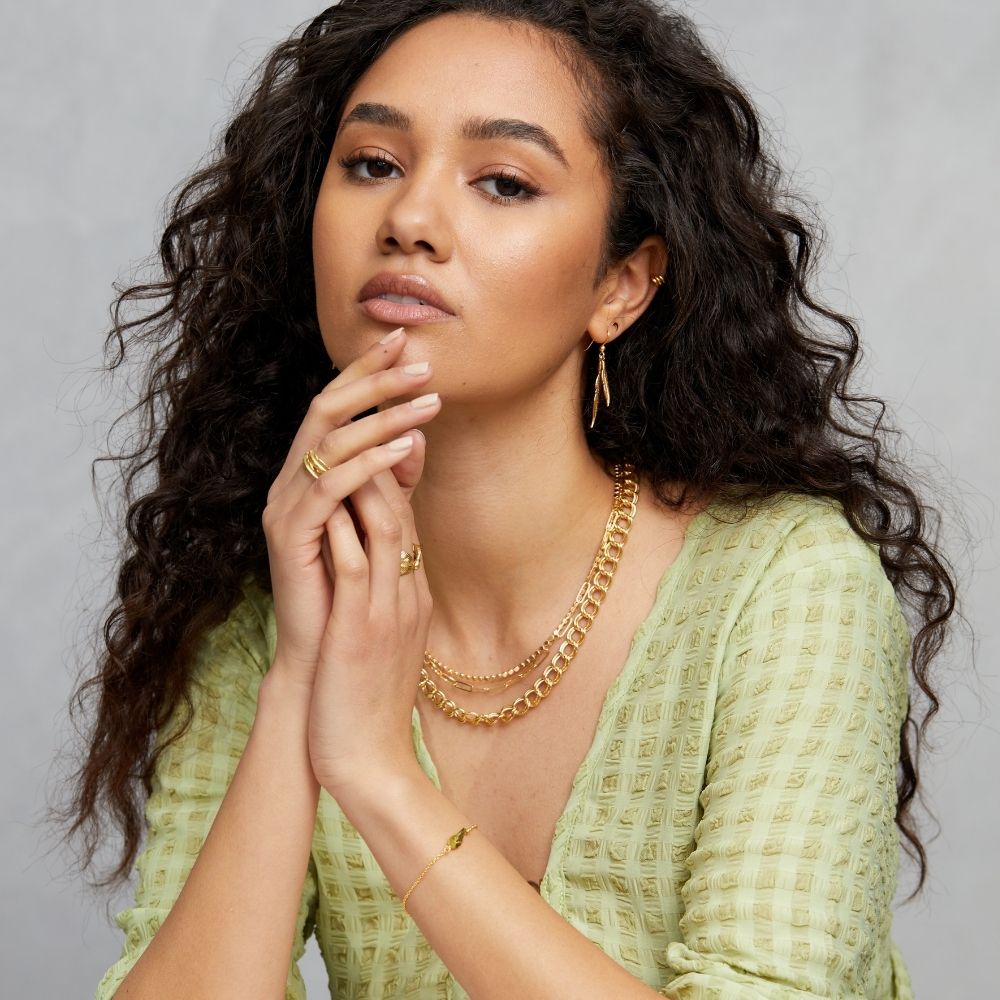 Woman in a green top wearing FIYAH yellow gold plated jewellery