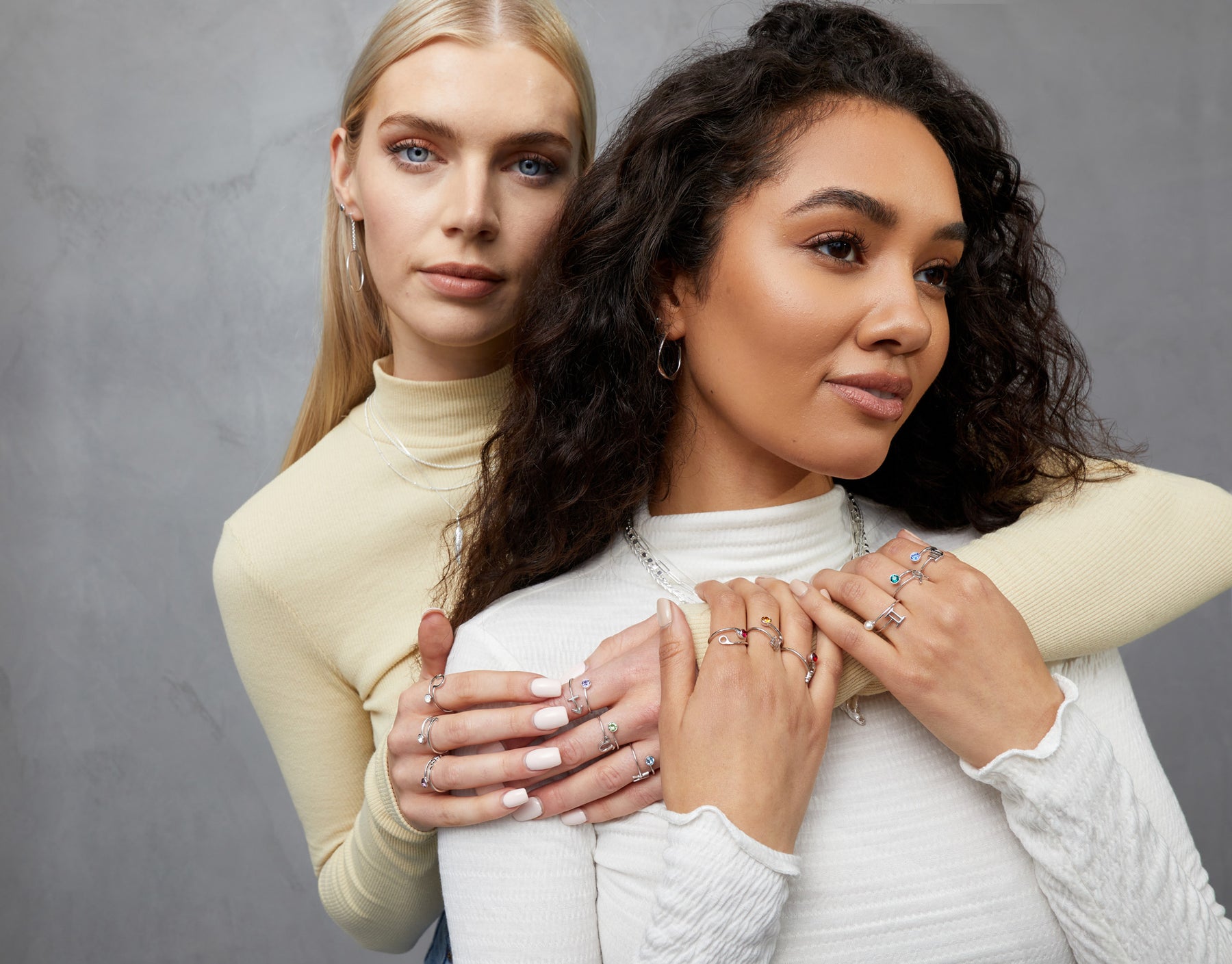 A close up image of two FIYAH models wearing the FIYAH Silver Zodiac Ring Collection and the FIYAH Silver Twisted Hoop Earrings