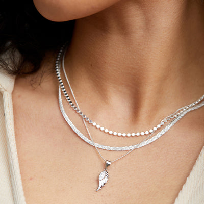 A close up of a woman wearing a FIYAH Silver Angel Wing Necklace